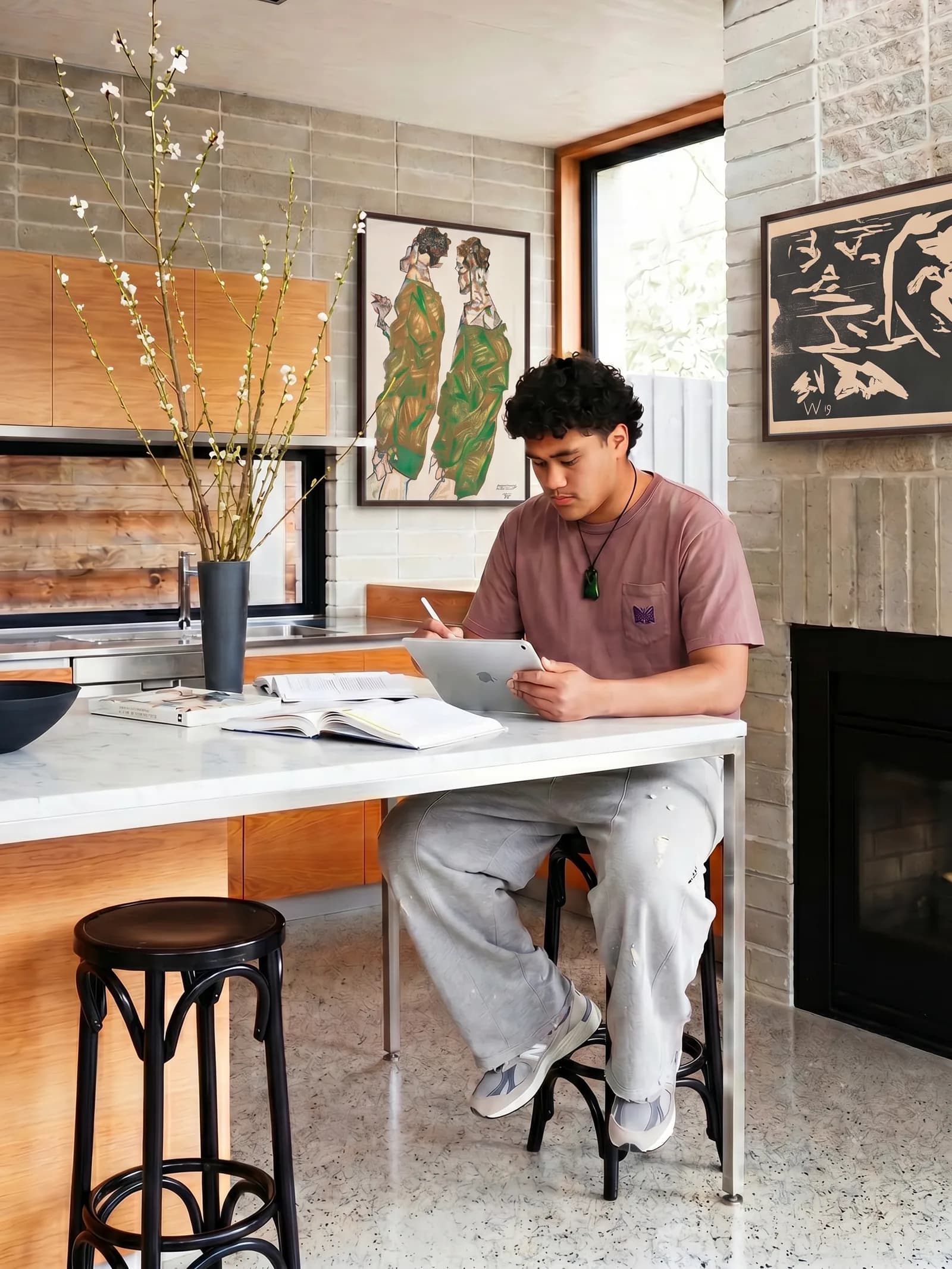 Student at a kitchen bench with tablet and an open notebook, warm wood interior, afternoon light