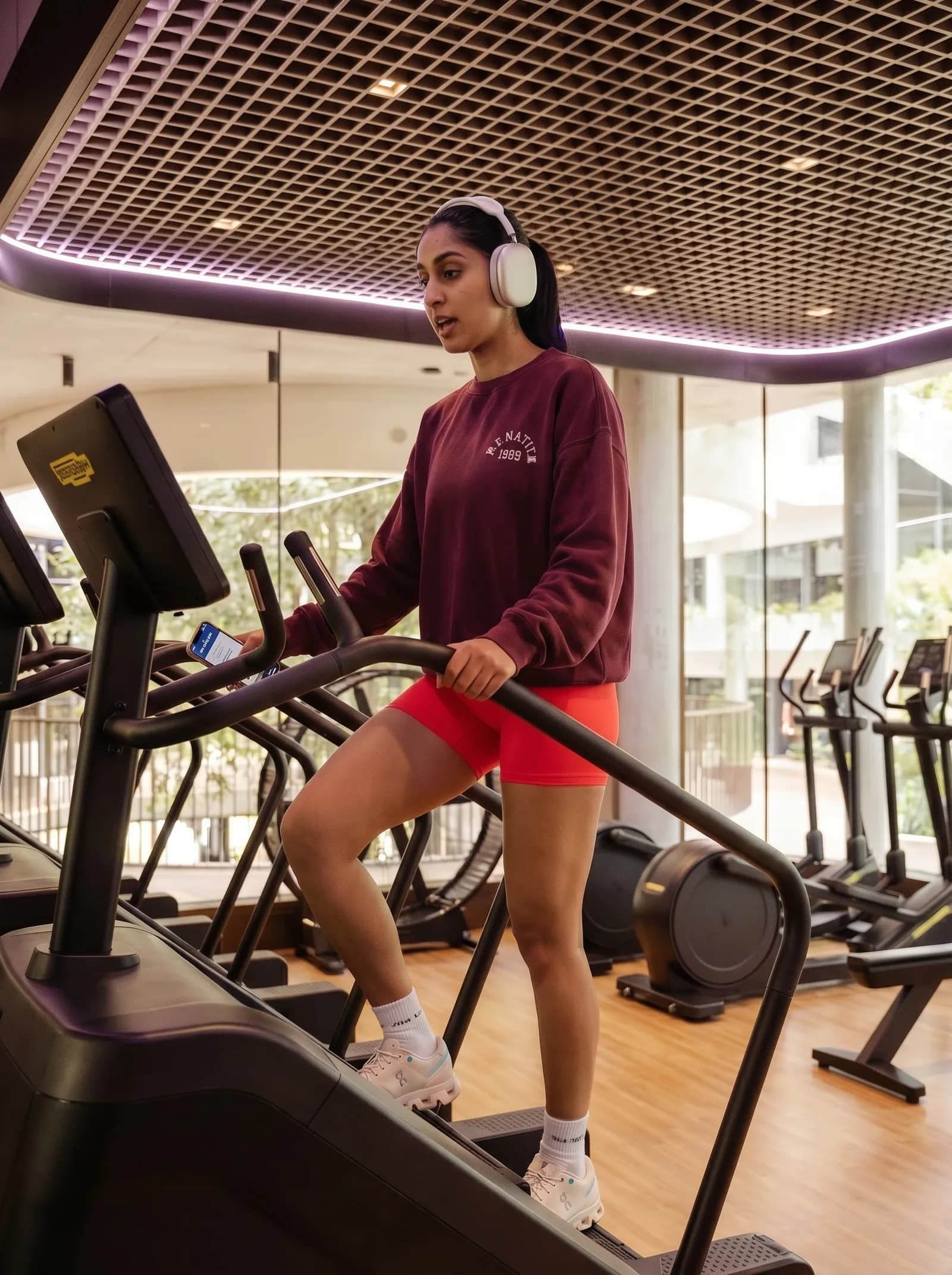 Registrar on a stair climber at the gym, headphones in, phone in hand